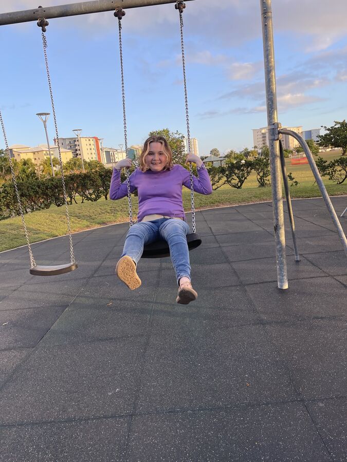 An Alfacare participant laughing on a swing at a Mackay playground
